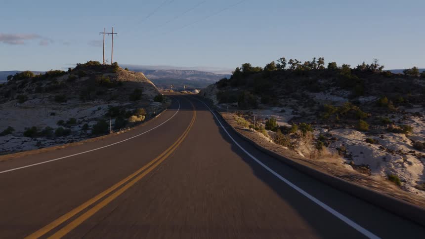 A first-person view from a vehicle driving along a winding scenic highway through a rocky desert canyon landscape at golden hour