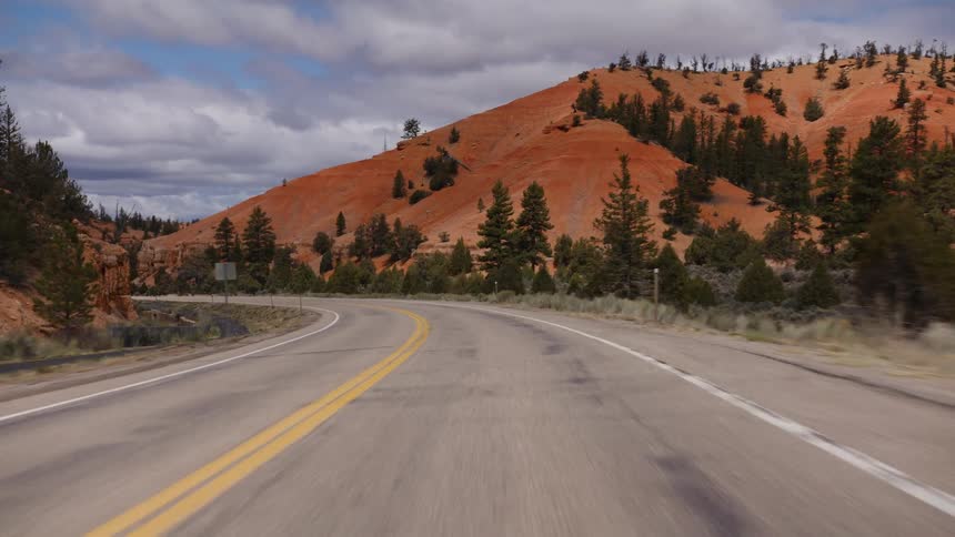 A scenic point-of-view drive on a winding highway through a stunning landscape of red rock mountains and pine trees