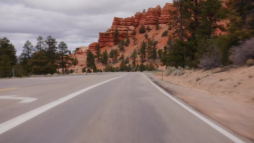 A scenic POV drive along a winding road through a majestic red rock canyon in Utah on an overcast day