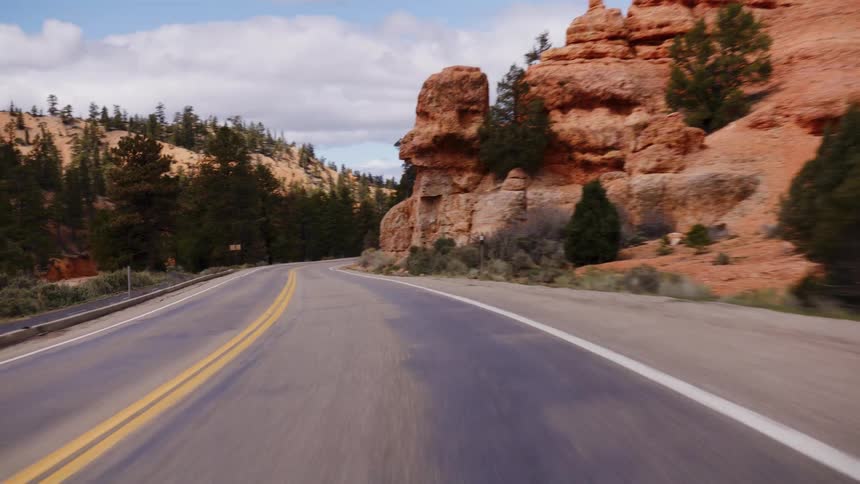 A scenic point-of-view drive on a winding road through a majestic red rock canyon with pine trees