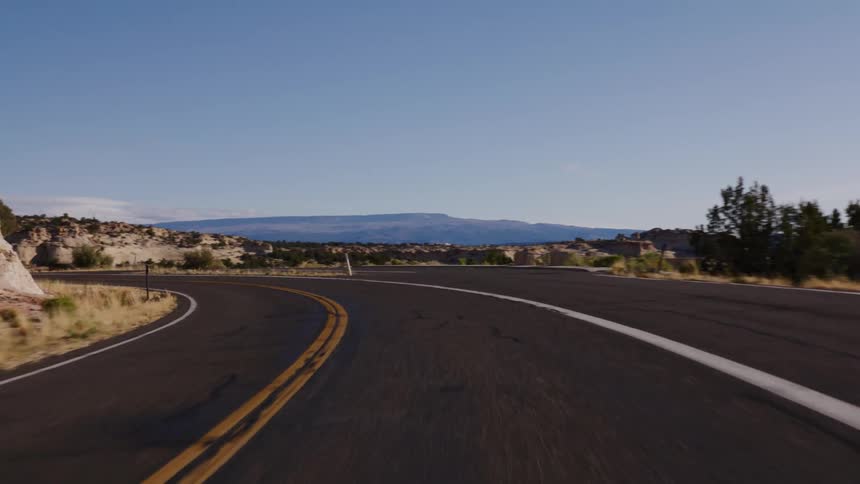 A point-of-view shot driving along a winding highway through a desert canyon landscape with red rock formations on a sunny day