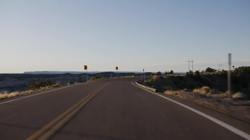 A point-of-view shot driving along a winding scenic byway through a desert canyon landscape at sunrise