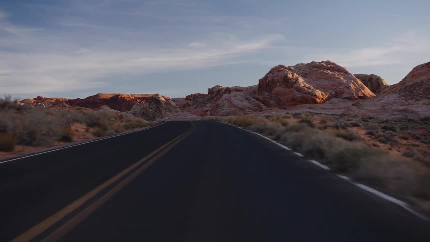 A first-person point-of-view shot driving along a winding desert highway through red rock formations during the golden hour
