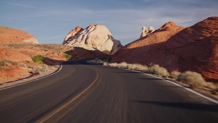 A point-of-view shot driving down a scenic, winding road through a desert landscape of red and white rock formations at golden hour