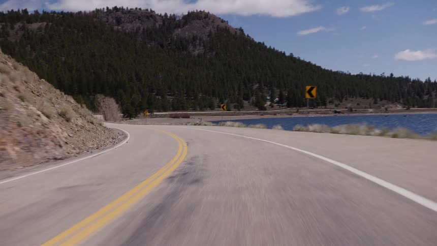 A slow-motion point-of-view shot driving on a winding mountain road alongside a scenic lake