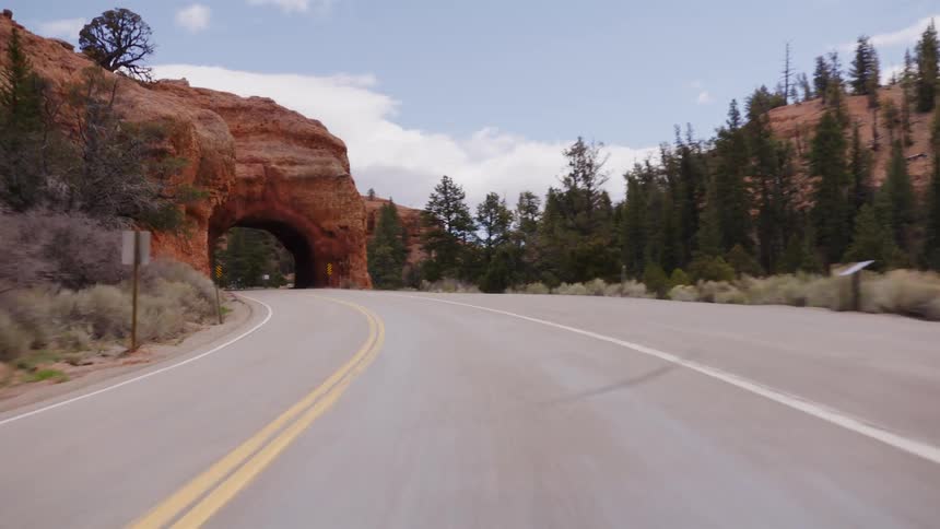 POV driving on a scenic highway, approaching and passing through a tunnel carved into a red rock formation