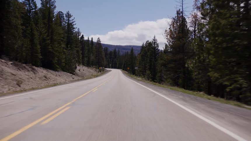 A scenic point-of-view drive along a winding highway through a mountain forest on a sunny day