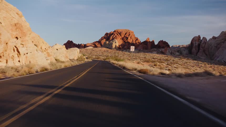 A scenic point-of-view drive down a winding desert road surrounded by vibrant red rock formations during the golden hour