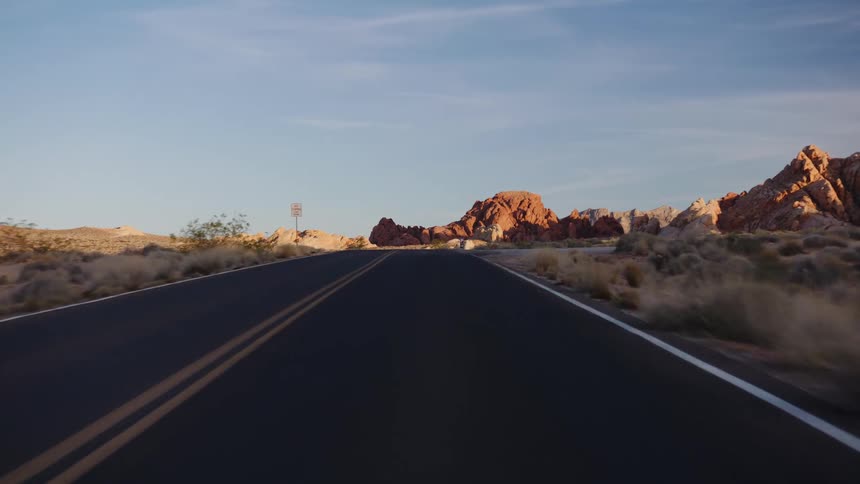 A scenic point-of-view drive along a winding desert highway surrounded by vibrant red rock formations at sunrise