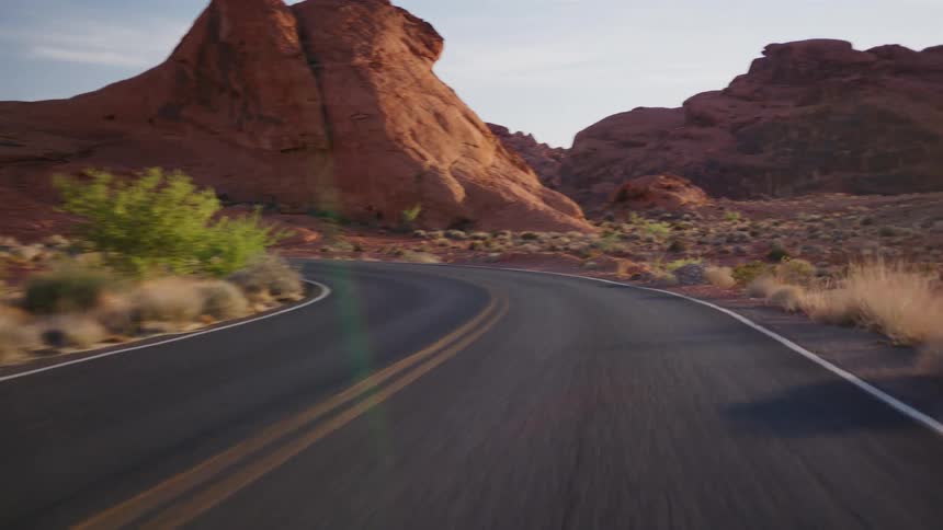 A smooth point-of-view drive on a winding asphalt road through a stunning desert landscape of red sandstone mountains at golden hour