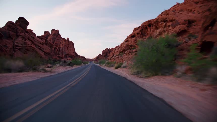 A point-of-view drive along a scenic highway winding through a majestic red rock canyon at dusk