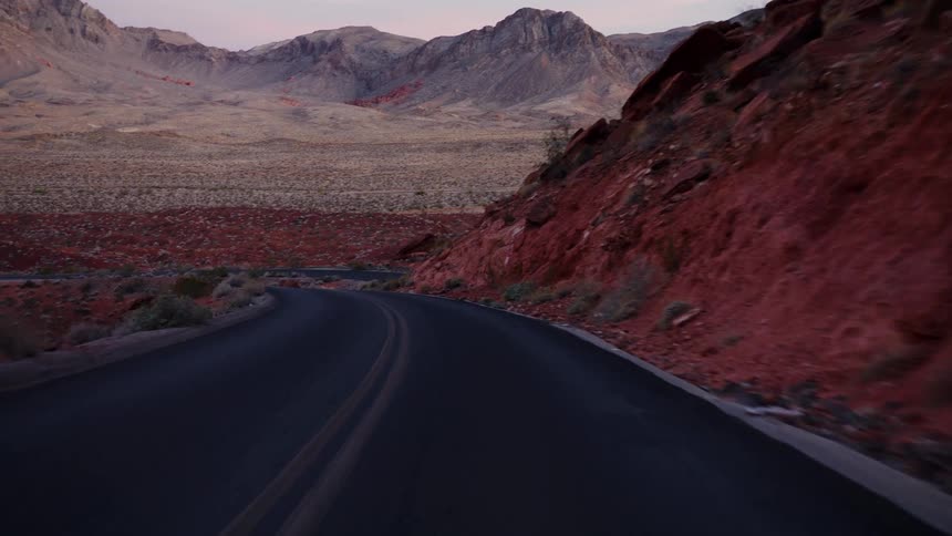 A smooth point-of-view shot driving along a winding road through a dramatic desert canyon landscape at dusk