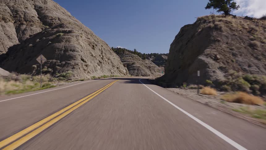 A scenic point-of-view drive along a winding asphalt road through a rugged mountain canyon on a sunny day