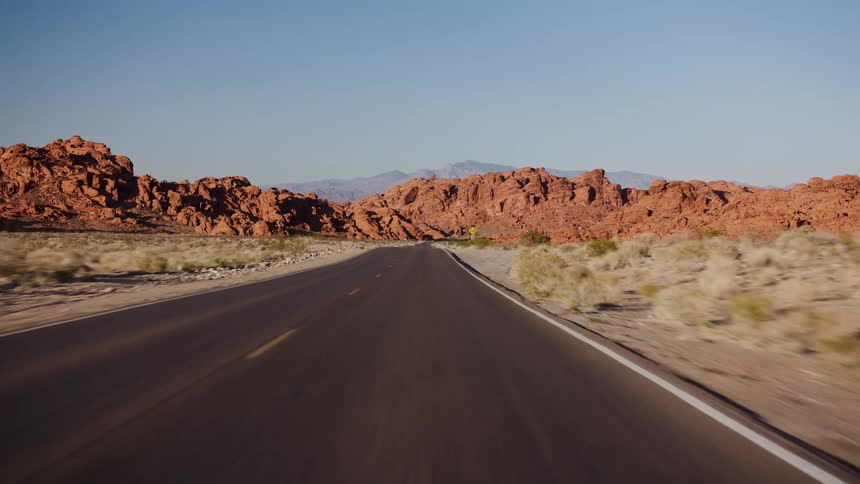 A scenic drive through a desert landscape with red rock mountains on a sunny day