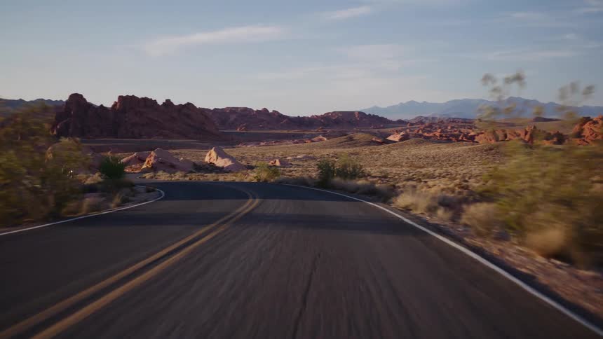 POV shot of a scenic drive along a winding road through a desert canyon landscape with red rock formations at sunrise