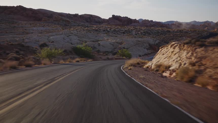 A smooth point-of-view shot driving along a winding road through a vast, rocky desert landscape during golden hour