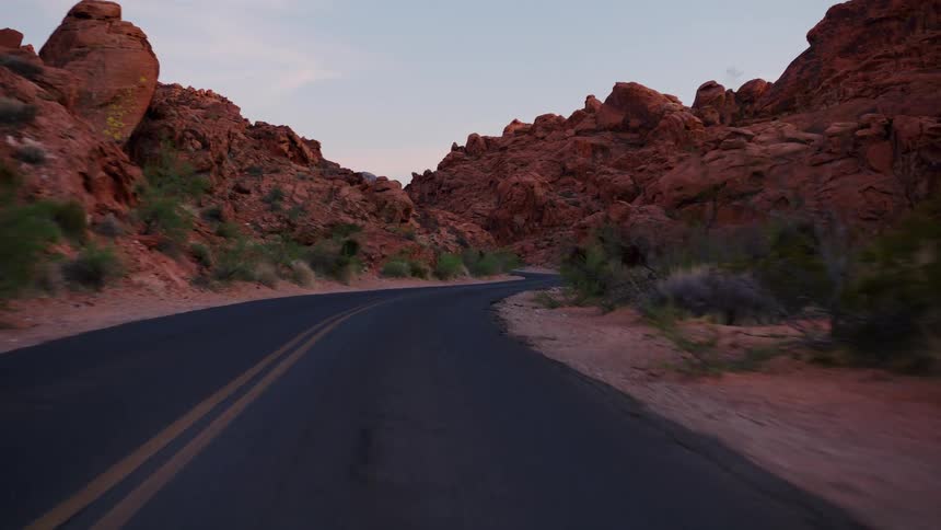 A serene point-of-view drive along a winding asphalt road through a magnificent red rock canyon at dusk