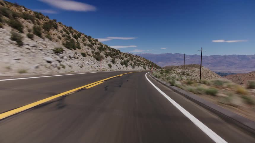 A scenic point-of-view drive on a winding mountain road through the desert with a vast blue sky