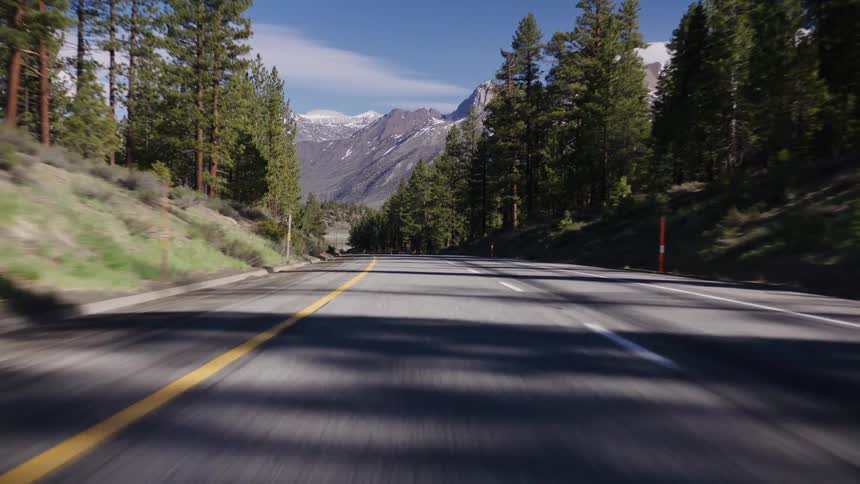 Point-of-view of a car driving along a scenic mountain highway towards snow-capped peaks under a clear blue sky