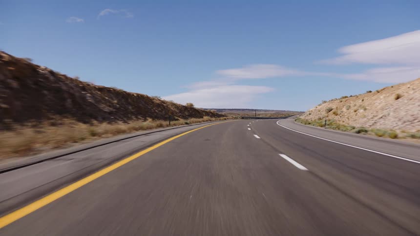 A fast-paced point-of-view shot driving along a curving highway through a desolate desert landscape under a clear blue sky