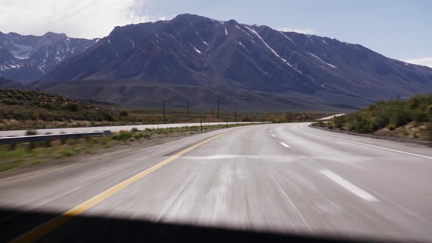 A fast-moving point-of-view shot travels along an empty highway and under a bridge towards a large, snow-capped mountain range