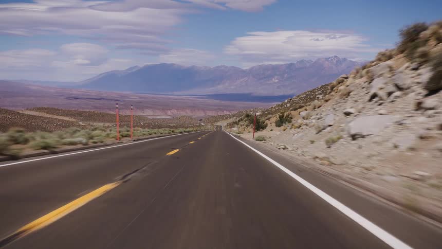 A point-of-view shot driving down a long, straight desert highway towards a vast valley and distant mountains