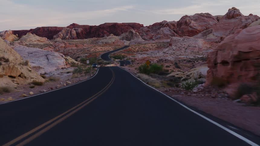 A scenic POV drive along a winding desert road through the Valley of Fire, passing bighorn sheep against a backdrop of colorful rock formations at dusk