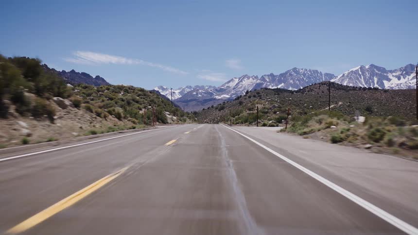 A point-of-view shot driving along a desert road with the magnificent snow-covered Sierra Nevada mountains in the distance