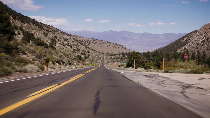 A point-of-view shot traveling down a long, straight highway through a beautiful mountain valley on a sunny day