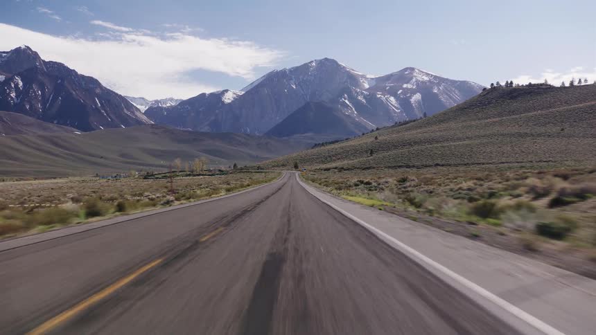 A scenic point-of-view drive on a remote highway heading towards majestic snow-capped mountains