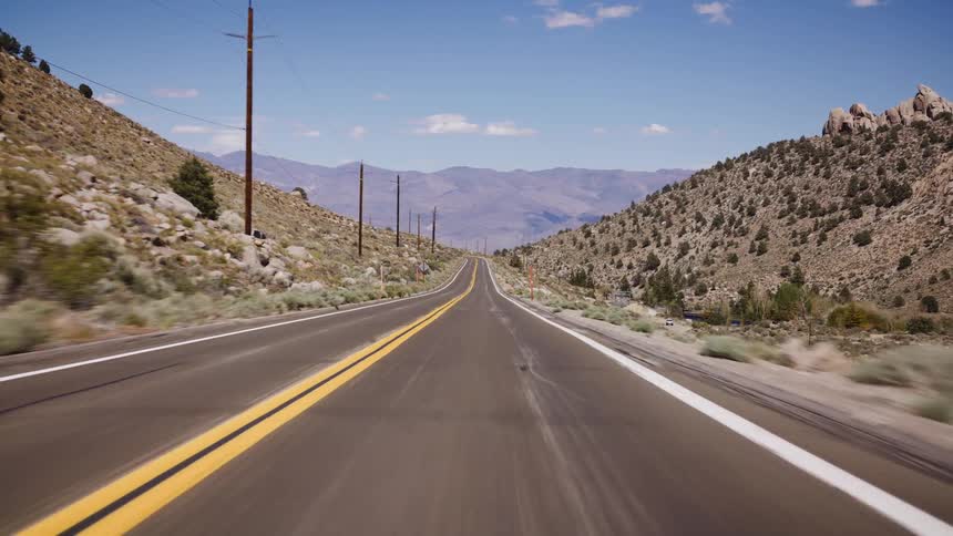 Experience the open road from a driver's perspective on a long, straight highway through a beautiful mountain pass