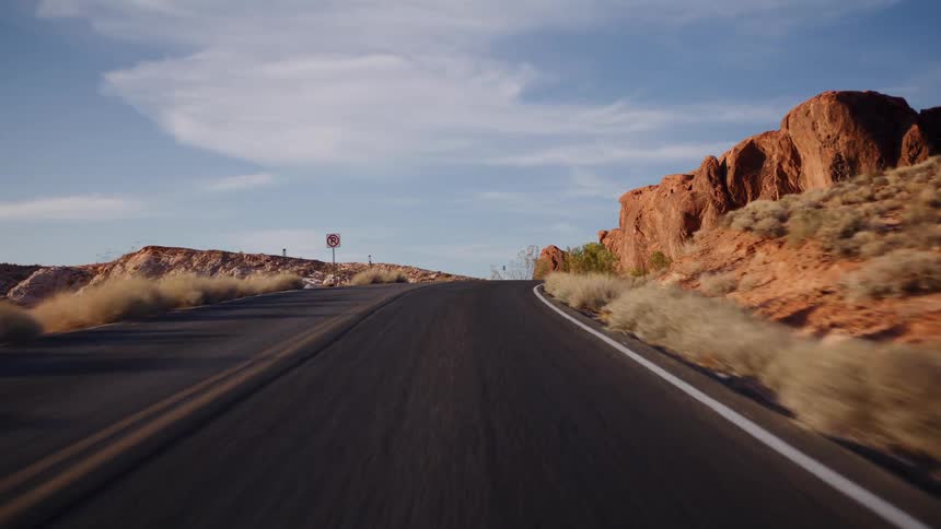 A point-of-view driving shot on a winding desert highway through red rock formations at golden hour