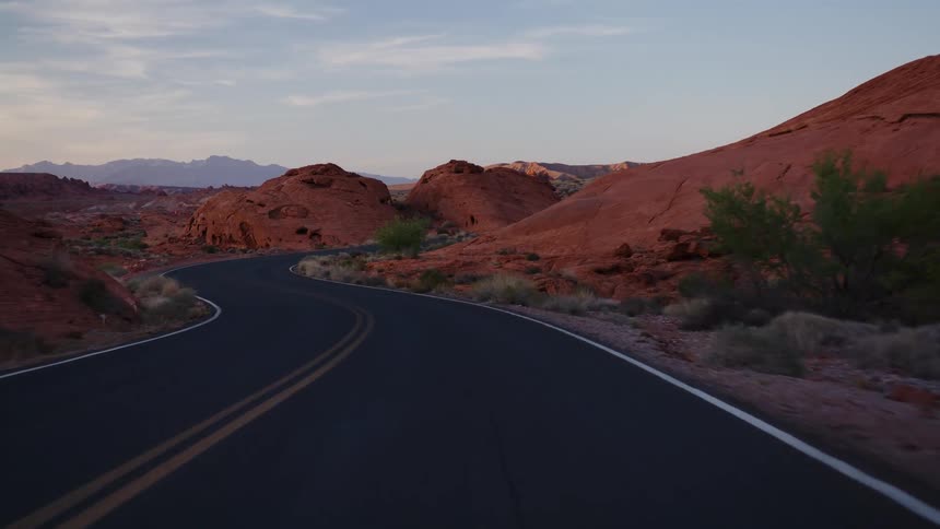 A point-of-view drive along a winding road through a majestic red rock desert canyon at sunrise or sunset