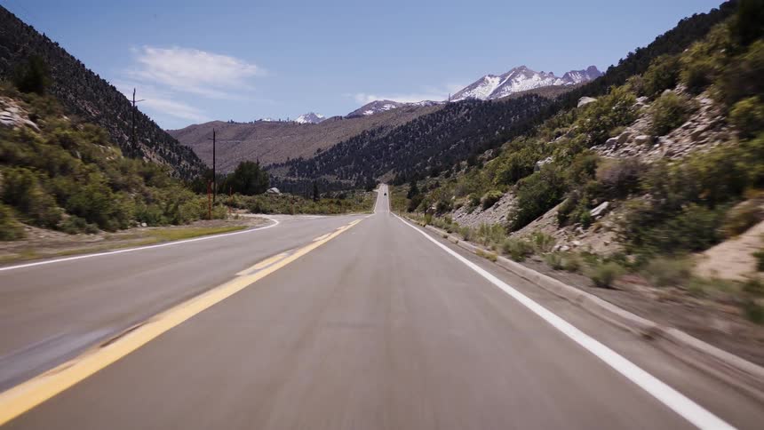 A smooth POV drive on a scenic highway through a mountain pass towards distant snow-capped peaks on a sunny day