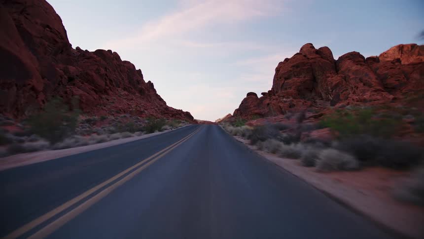 An immersive point-of-view drive along a scenic desert highway surrounded by majestic red rock formations at dusk
