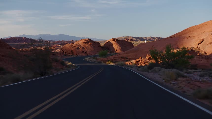A point-of-view drive along a winding road through a desert landscape of red rock formations during the golden hour