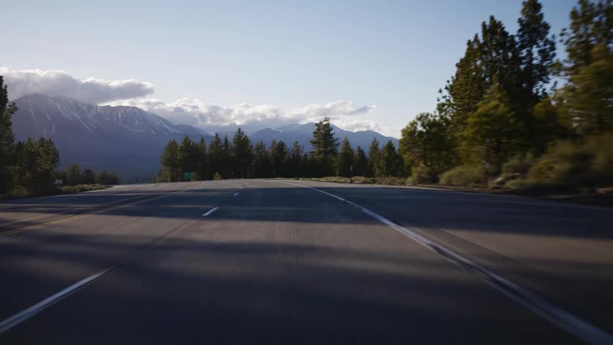 A scenic point-of-view drive on an empty mountain road towards snow-capped peaks during a beautiful sunrise