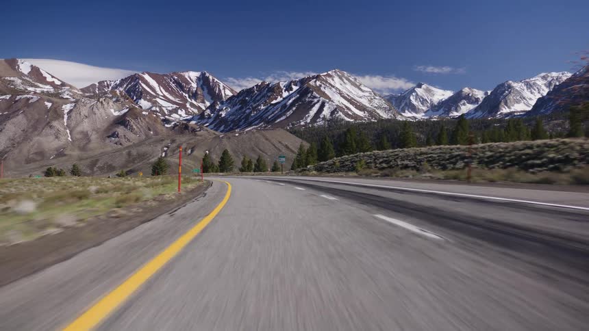 A point-of-view shot driving on a scenic highway towards the majestic snow-capped Sierra Nevada mountains on a clear sunny day