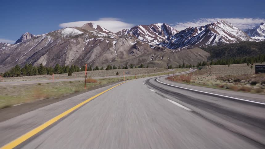 A scenic point-of-view drive on a curving highway towards the majestic snow-capped Sierra Nevada mountains on a sunny day