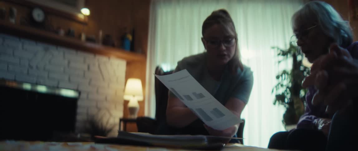 A young woman explains a document with charts and graphs to an older woman in a cozy living room