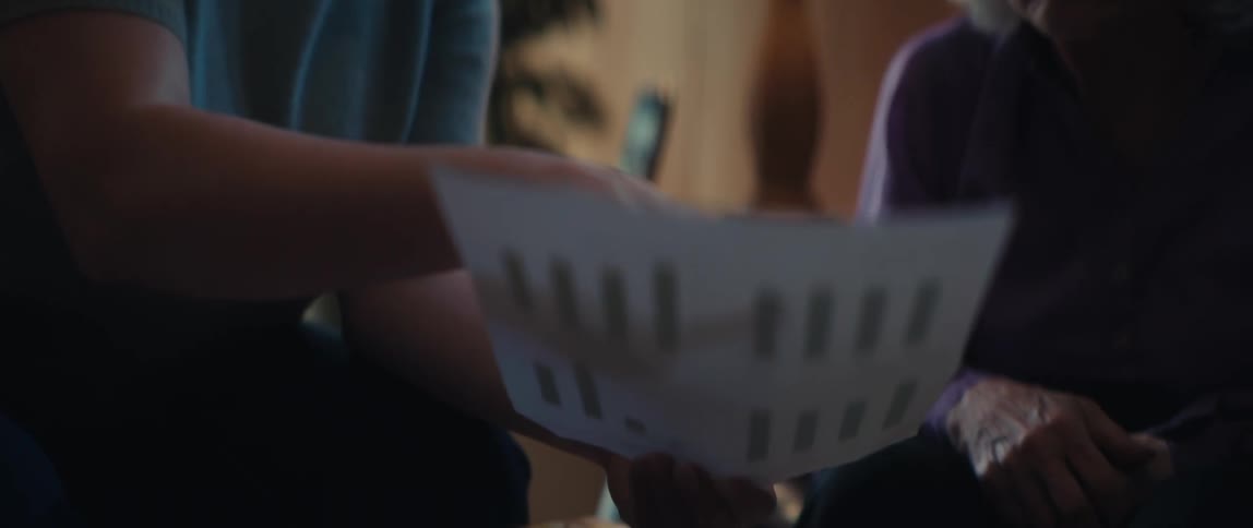 A young woman with glasses explains a financial report with bar charts to an older woman in a warmly lit room