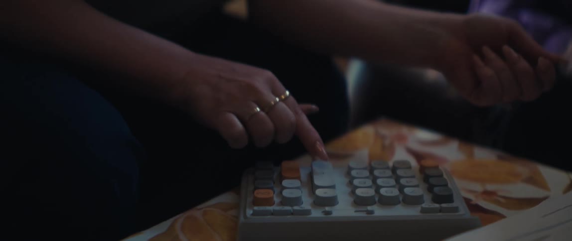 A rack focus shot moves from financial documents and a vintage calculator to an elderly woman reviewing her finances