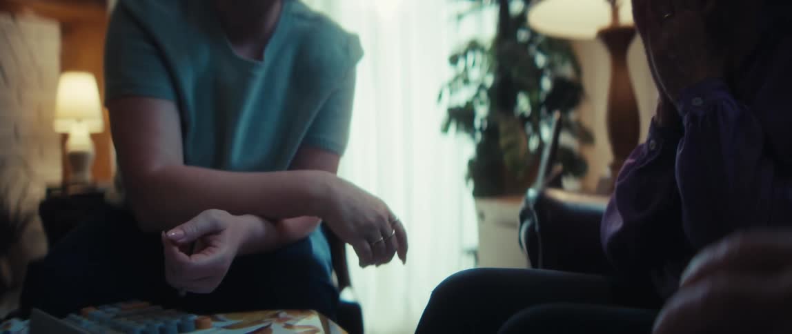 A caregiver shakes hands with an elderly woman and man during a home visit in a softly lit living room