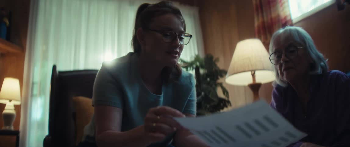 A caring young woman patiently explains the details of a document to an elderly woman in a softly lit living room