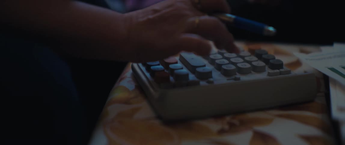 A financial advisor uses a calculator to review an elderly woman's budget in a dimly lit room