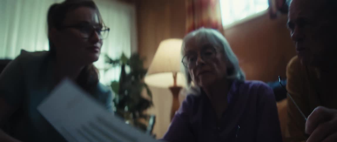 An older woman with glasses listens attentively to a consultant during a financial planning meeting at home