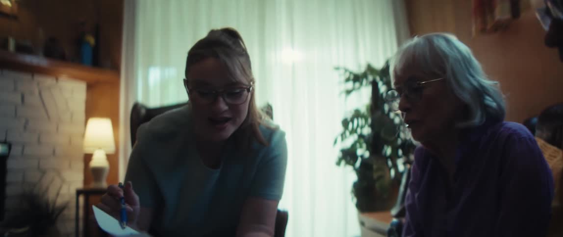 A caring young woman helps a senior couple review paperwork in their dimly lit living room