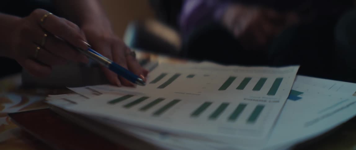 Close-up slow-motion shot of a woman's hand with rings pointing a pen at a business report with bar graphs