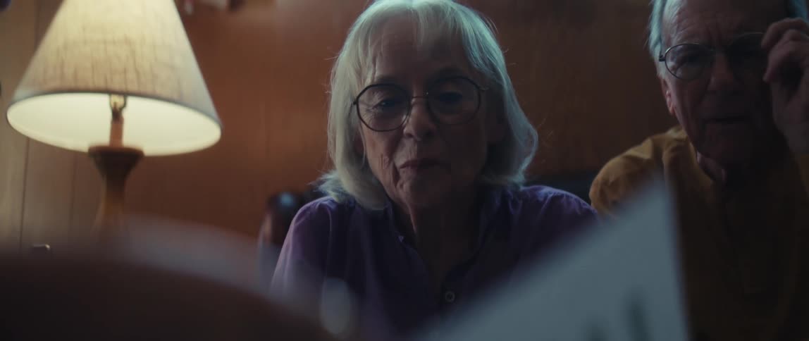 A financial consultant reviews a positive performance report with a smiling elderly couple in their living room