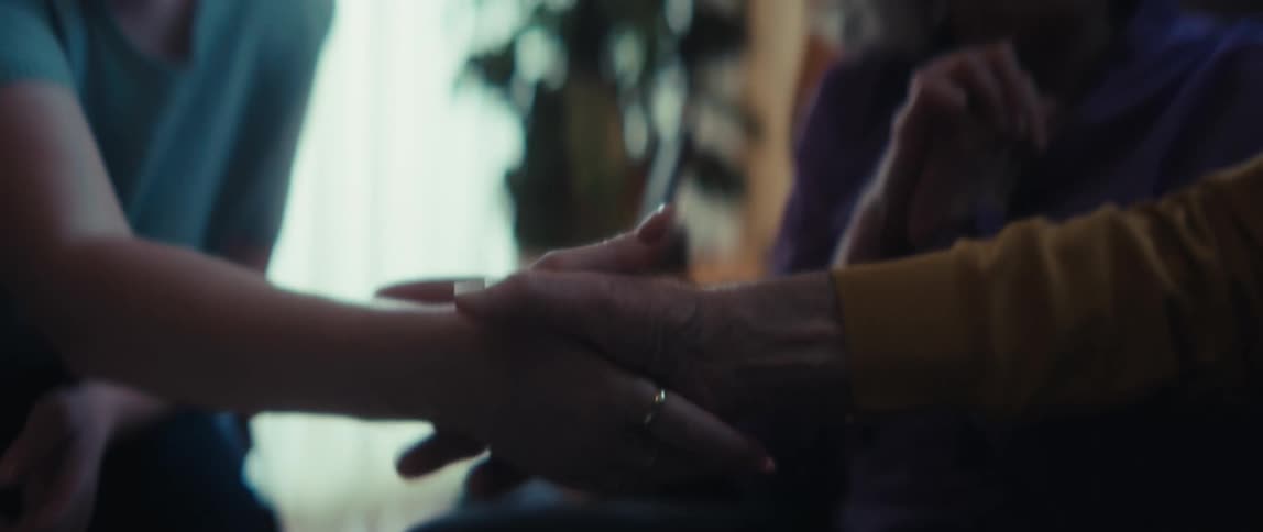A young woman and an elderly woman share a supportive conversation, concluding with a warm handshake in a cozy living room